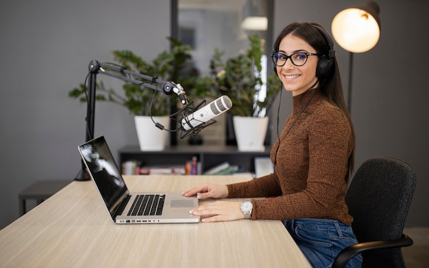 Side view of smiley woman on the radio with microphone and laptop