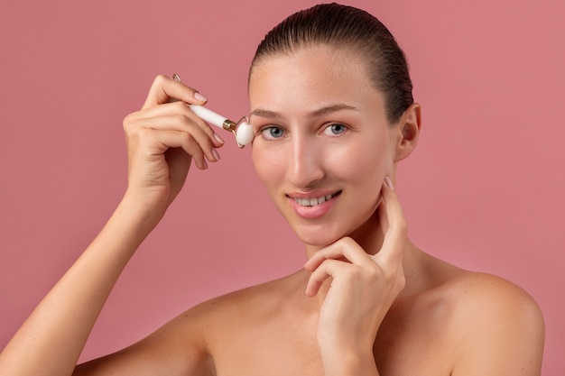 Free photo side view smiley woman using face roller