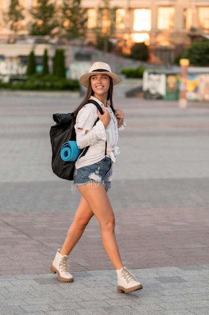 Side view of smiley woman with hat carrying backpack while traveling alone