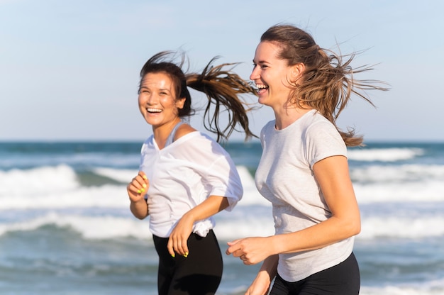 Side view of smiley women running together on the beach