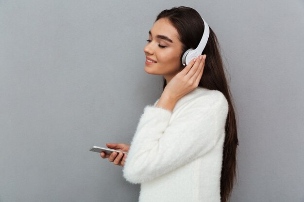 Side view of smiling brunette woman in sweater and headphones