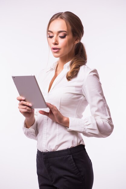 Side view of a smiling confident woman standing and using digital tablet isolated against gray wall