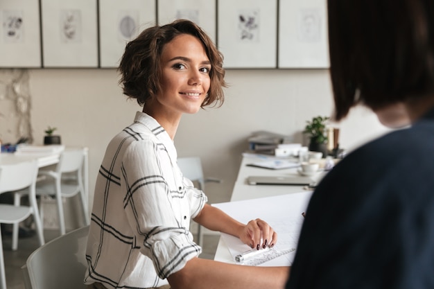 Side view of smiling curly business woman sitting by table