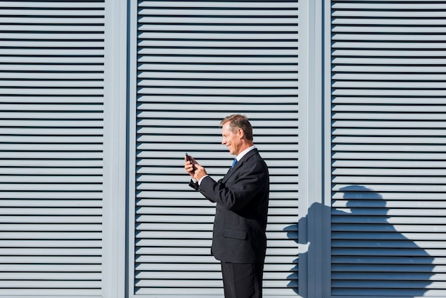 Foto gratuita vista laterale di un uomo d'affari maturo sorridente che utilizza cellulare all'aperto