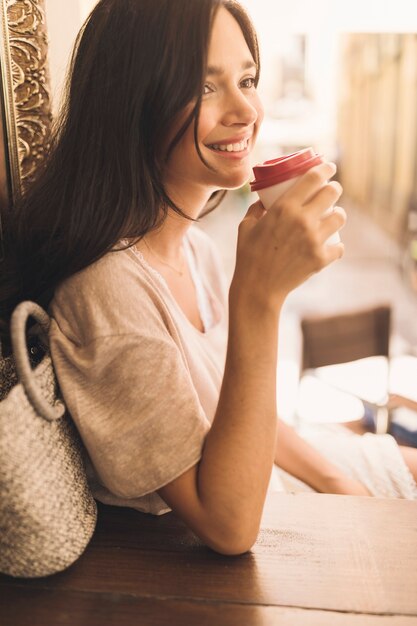 Side view of smiling woman drinking disposable coffee