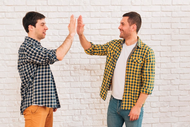 Side view of a smiling young male friends giving high five to each other