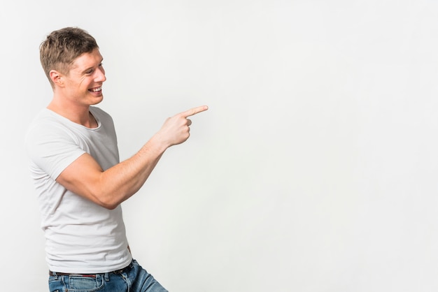 Side view of a smiling young man pointing her finger at something against white background