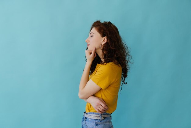 Side view of smiling young redhead woman girl in yellow sweater posing isolated on blue turquoise background in studio People lifestyle concept Hold hands crossed looking aside