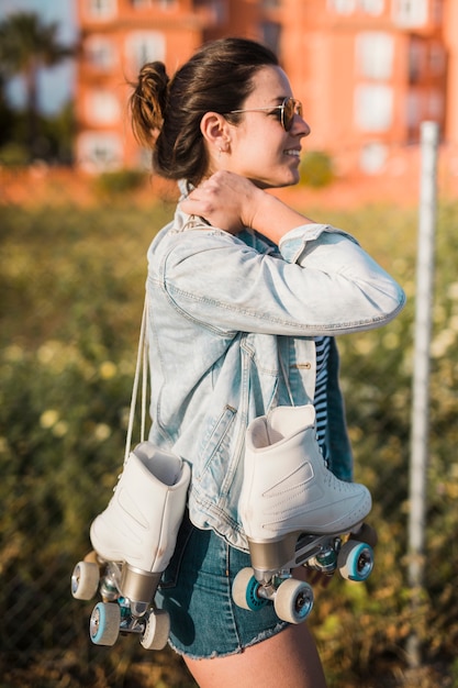 Side view of a smiling young woman holding roller skate on her shoulder