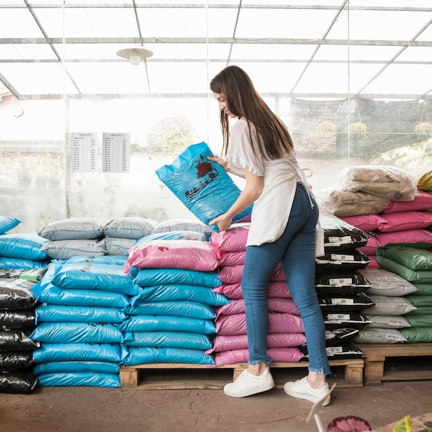 Side view of a smiling young woman stacking plastic sacks in greenhouse