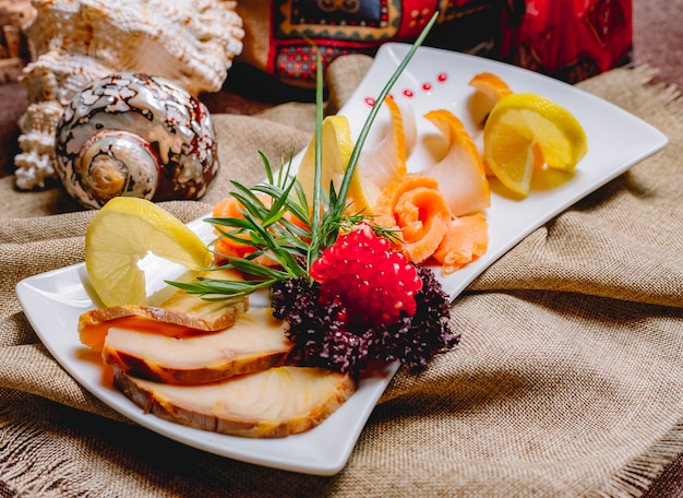 Free photo side view smoked fish plate balyk salmon with herbs pomegranate and lemon slices