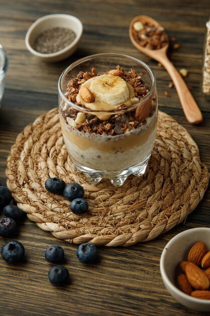 Side view of smoothie with banana almond walnut milk peanut butter in glass on trivet with blackthorn almond on wooden background