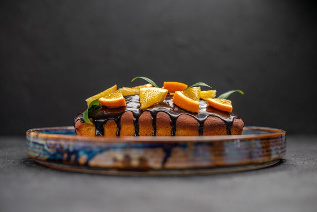 Side view of soft cake decorated with orange and chocolate on dark table