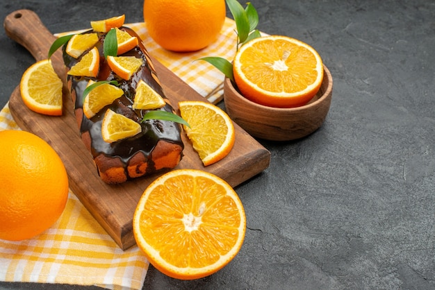 Вид сбоку на мягкие торты целиком и нарезанные апельсины с листьями на темном столе