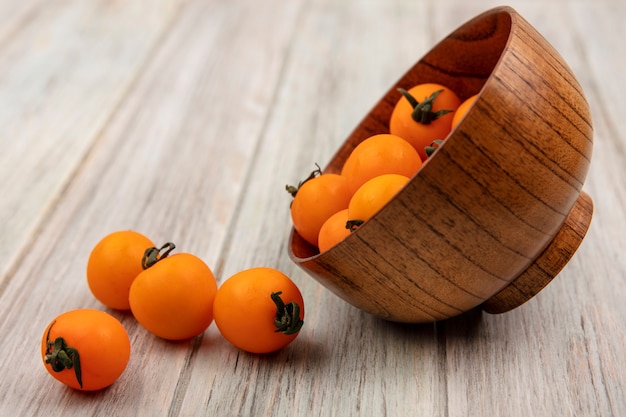 Side view of soft orange tomatoes falling out of a wooden bowl on a grey wooden surface