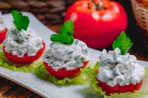 Free photo side view of sour cream yogurt with cucumbers galic and herbs on fresh tomatoes topped with parsley on a plate