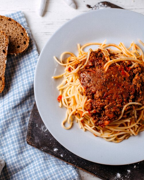 Side view of spaghetti bolognese on white plate on a wooden cutting board