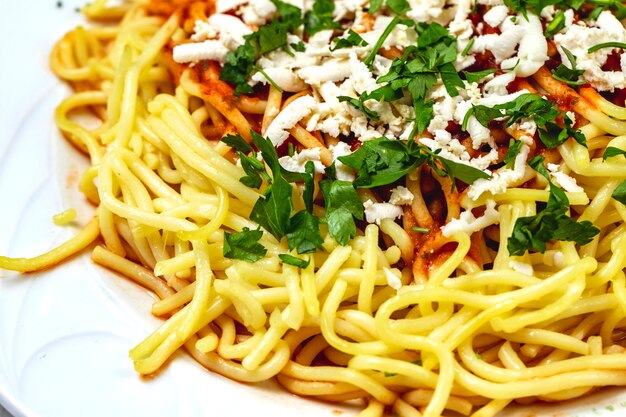 Вид сбоку спагетти болоньезе с мясным фаршем, томатным соусом, белым сыром и зеленью на тарелке