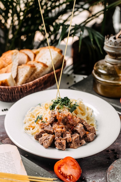 Side view of spaghetti with pieces of meat and tomato on a wooden board