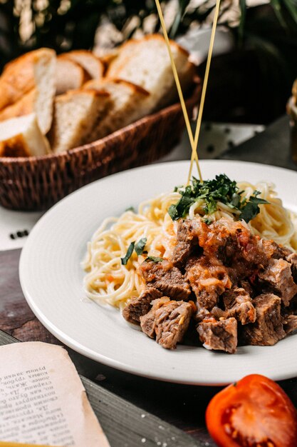 Side view of spaghetti with pieces of meat and tomato on a wooden board