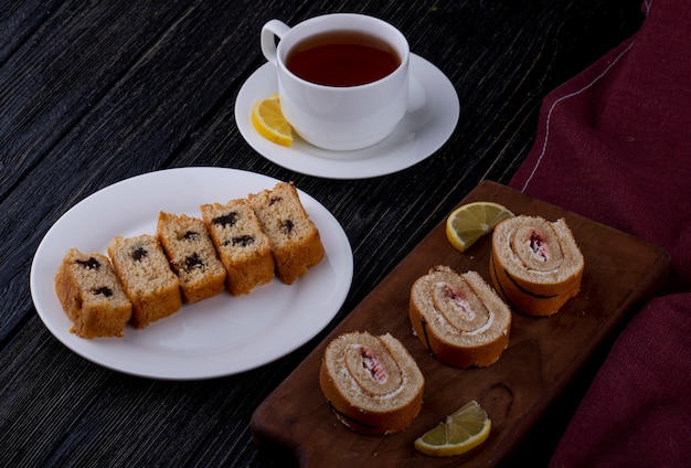 Side view of sponge cake slices with chocolate and raspberry jam on a wooden board served with a cup of tea