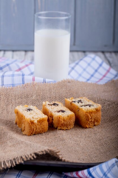 Side view of sponge cake slices with chocolate on sackcloth with a glass of milk