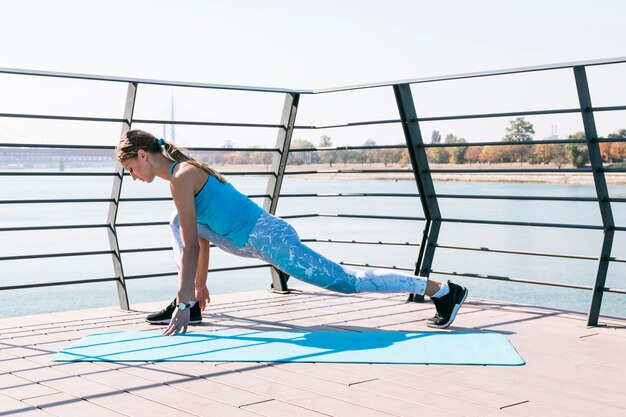 Side view of sportive young woman exercising on bridge near the lake