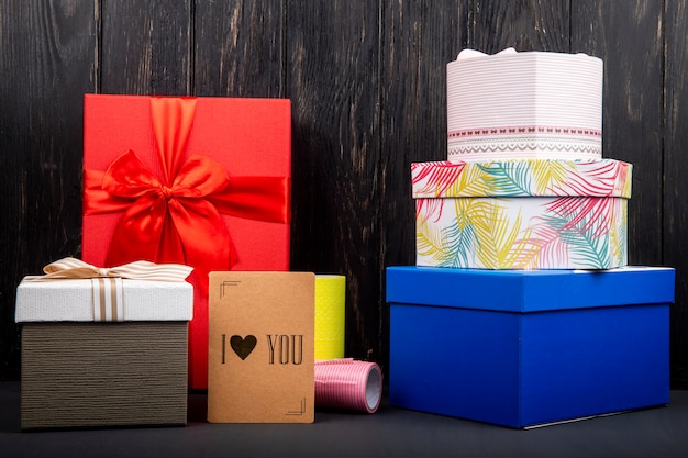 Free photo side view of a stack of colorful present boxes and a small i love you card at dark wooden table