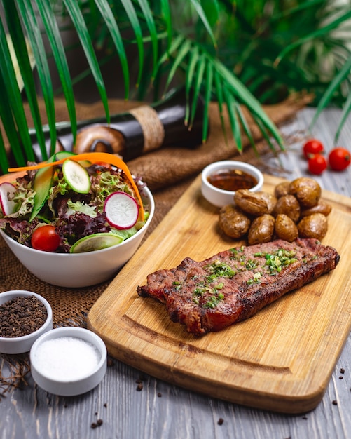 Вид сбоку стейк с красным салатом на гриле с салатом из редьки из огурцов и помидоров и жареным картофелем на столе