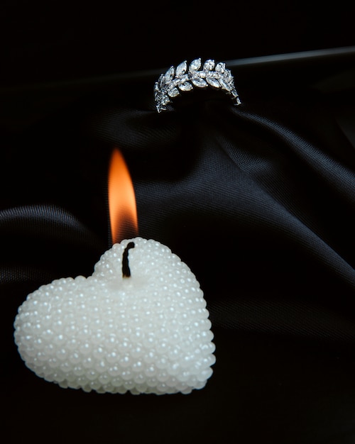 Side view of sterling silver ring with diamonds and with burning decorative candle in a heart shape on black wall
