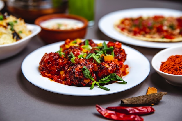 Side view stewed meatballs with tomato sauce bell pepper spring onion and mint on a plate