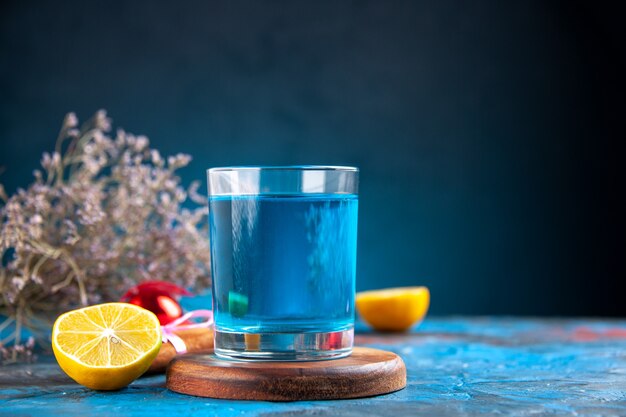 Side view of a still water in a glass on wooden cutting board and lemons cinnamon limes conifer cone decoration accessory on blue background