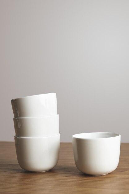 Side view straight shaped blank white simple coffee cups in pyramide on thick wooden table isolated