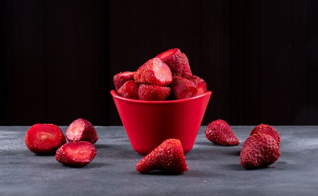 Side view strawberries in bowl with others forming circle around on dark table