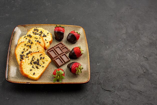 측면 뷰 딸기와 케이크 케이크, 초콜릿으로 덮인 딸기는 테이블 왼쪽에 있는 회색 접시에 있습니다.