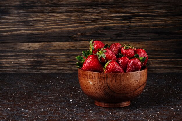 Side view strawberry in a bowl on wooden background