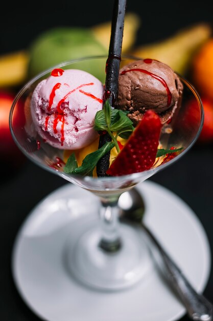 Вид сбоку шариков клубничного и шоколадного мороженого в стеклянной вазе, украшенной мятой