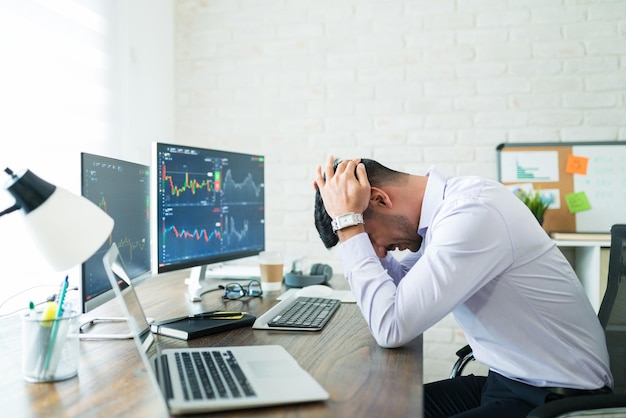 Side view of stressed young broker sitting with head in hands at desk while working from home