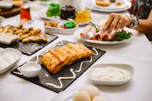 Side view of stuffed pancakes with meat and cream sauce on a black board