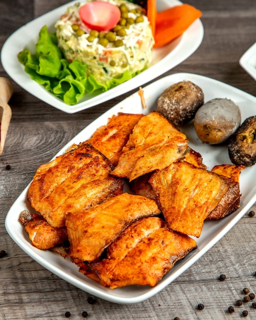 Side view of sturgeon kebab with baked potato served with vegetable salad on a wooden table