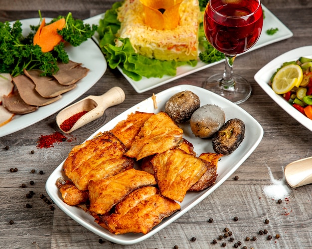 Side view of sturgeon kebab with baked potato on a white plate on a wooden table