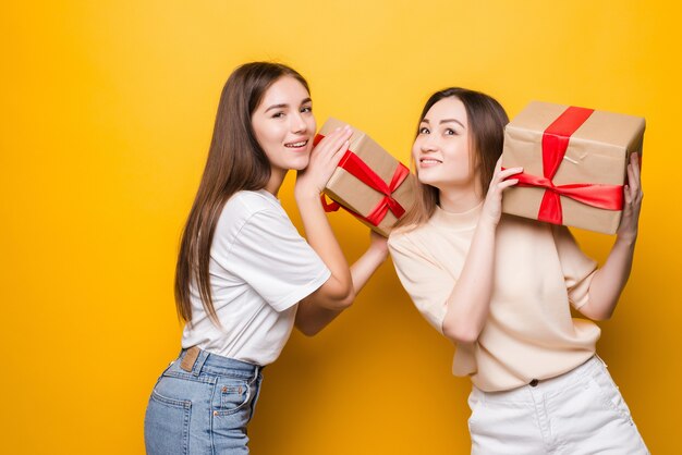 Side view of surprised young women hold present box with gift ribbon bow isolated on yellow wall . Women's Day birthday, holiday concept.