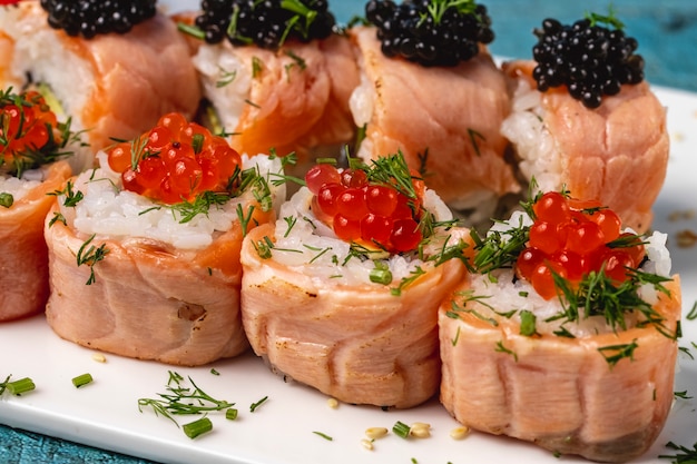 Free photo side view sushi roll with baked salmon dill red and black caviar on a plate