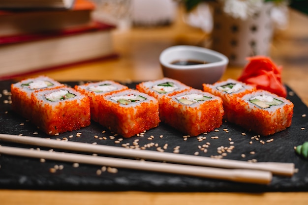 Side view of sushi set rolls with crab meat cream cheese and avocado in caviar of flying fish with soy sauce on a black board