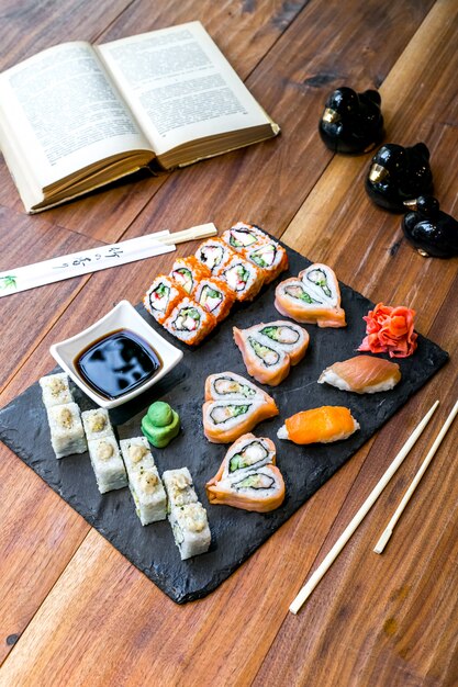 Side view sushi set rolls with soy sauce ginger and wasabi on a plate and with a book on the table