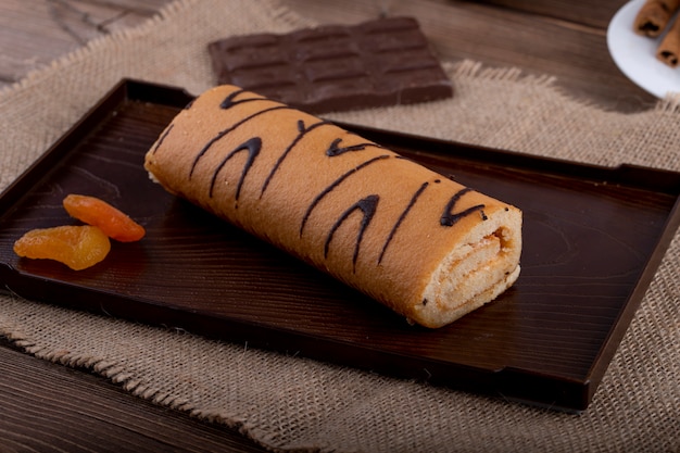 Free photo side view of swiss roll with apricot jam on a black board