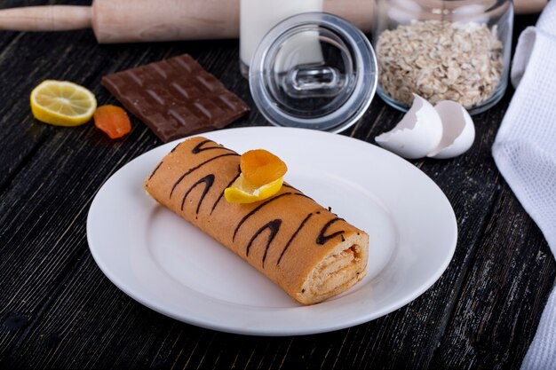 Side view of swiss roll with apricot jam on a white plate