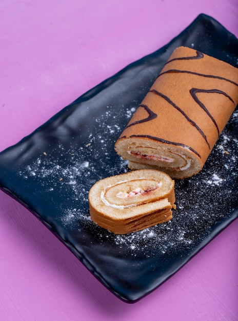 Free photo side view of swiss roll with whipped cream and raspberry jam on a black board