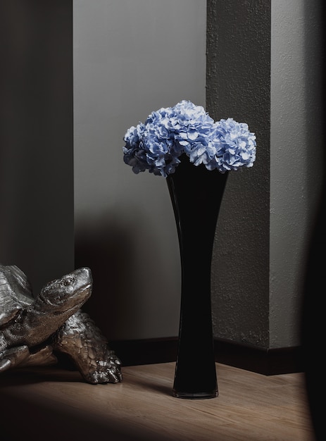 Foto gratuita vista laterale del vaso nero di vetro alto con i fiori blu su un pavimento di legno