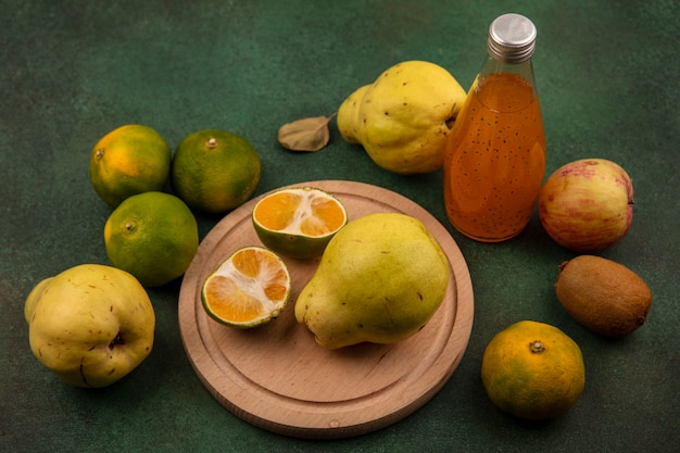 Side view tangerine slices on a stand with pears apple kiwi and a bottle of juice on a green wall